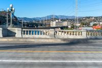 a view down a paved city street with some hills in the background near a bridge and water