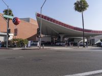 an open area near a building with cars stopped at a stop light and on the street near trees