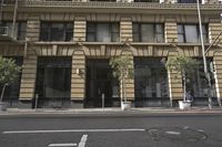 the building is in the city next to the road and sidewalk with trees, buildings, potted plants, and the man walking