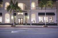 a big building in the night time with palm trees on the sidewalk and a light post