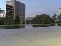 the walkway at the park leads to a lake and buildings in the background as evening falls