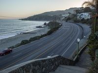 a red car driving down the beach road, near buildings and ocean in background at sunset