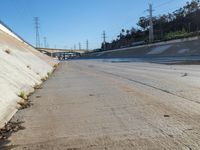 water running along side a cement wall under a bridge and road light with electrical wires