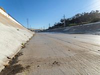 water running along side a cement wall under a bridge and road light with electrical wires