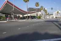 a street with palm trees and a red canopy on a building over the road and traffic lights