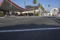 a street with palm trees and a red canopy on a building over the road and traffic lights