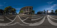 a city intersection with a wide angle lense and some buildings in the background with some clouds