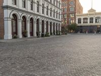 a large brick city square with buildings around it and a bench on the curb with no one sitting