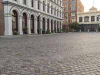 a large brick city square with buildings around it and a bench on the curb with no one sitting