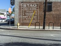 a yellow fire hydrant on a sidewalk in front of a building with the stag provisions sign written on it