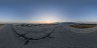 a fish - eye view of a road from a vehicle window at dusk with the sun setting in the background