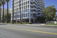 the building is tall and slender, as seen from a street corner in front of palm trees