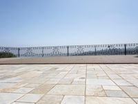 an empty patio in front of a railing and lake view looking out onto the water