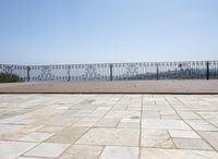 an empty patio in front of a railing and lake view looking out onto the water