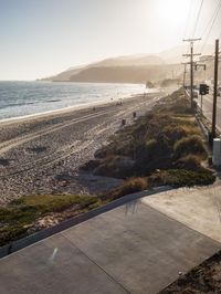 a street is shown next to the ocean shore on a sunny day, and some power lines are also visible in the foreground