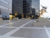 a concrete walkway in front of a glassy skyscraper building with people sitting outside on the side