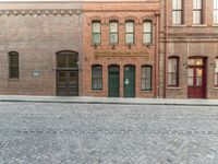 an empty brick road in an old town with a green door and a sidewalk with cobblestone