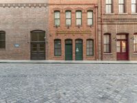 an empty brick road in an old town with a green door and a sidewalk with cobblestone