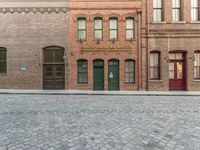 an empty brick road in an old town with a green door and a sidewalk with cobblestone