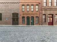 an empty brick road in an old town with a green door and a sidewalk with cobblestone