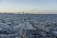 rocky shoreline near a body of water and lots of ships in the distance at dusk