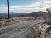 a dirt road running through the countryside with power lines overhead and hills in the distance