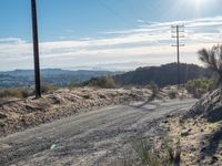 a dirt road running through the countryside with power lines overhead and hills in the distance