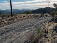 a dirt road running through the countryside with power lines overhead and hills in the distance