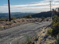 a dirt road running through the countryside with power lines overhead and hills in the distance