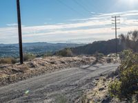 a dirt road running through the countryside with power lines overhead and hills in the distance