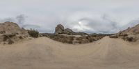 a panoramic view of an old dirt road at a desert park with mountains and clouds