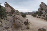 dirt trail through the middle of large rock formations in the middle of arid desert area