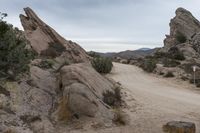 dirt trail through the middle of large rock formations in the middle of arid desert area