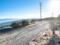 a person riding a motorcycle on a dirt road near a power line and mountains of greenery