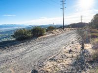 a person riding a motorcycle on a dirt road near a power line and mountains of greenery