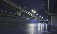 people walk in the street at night on an empty concrete walkway, near a highway bridge