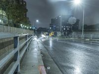 a wet street at night with cars passing by in the rain, and a person standing on a sidewalk, under a streetlight