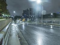 a wet street at night with cars passing by in the rain, and a person standing on a sidewalk, under a streetlight