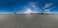 a large open field with a sky and clouds in the background and a tree on the ground near by