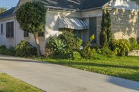 a house on a sidewalk that is lined with lots of bushes and trees outside the house is brick