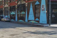 an empty street in front of a store that is painted with colorful graffiti and has two cars parked on the side of it