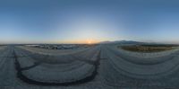 a sun setting behind a desert mountain on top of a paved road and a half way highway