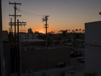 a sunset view of some power lines and cars parked at an intersection with palm trees