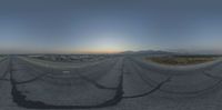 a fisheye lens image of a paved area with trees and mountains at sunset while the sun is setting