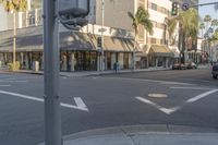 a white car driving through an intersection of town next to palm trees and shops at a intersection with a sign pointing left