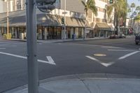 a white car driving through an intersection of town next to palm trees and shops at a intersection with a sign pointing left