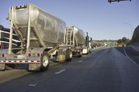 two tanker trucks traveling along a highway under an overpass sign on a sunny day