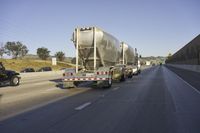 two tanker trucks traveling along a highway under an overpass sign on a sunny day