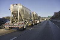 two tanker trucks traveling along a highway under an overpass sign on a sunny day