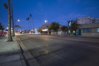 a city street with empty roads and palm trees at twilight, and traffic lights in the distance